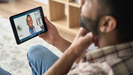 A man holding a tablet device has a telemedicine visit with a doctor.